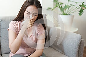 Asian Cute of  girl having  flu season and sneeze using paper tissues sitting on sofa at home, Health and illness concepts