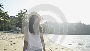 Asian cute girl wearing straw hat and casual dress walking on the beach under sunlight in the morning.
