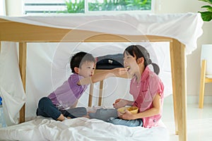 Asian cute little boy feeding snack to his sister sibling while sitting in a blanket fort in living room at home for perfect