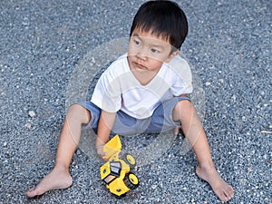 Asian cute little child boy playing yellow car toy outdoor with dirty foot