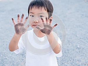 Asian cute little child boy showing dirty black hands while playing outdoor.