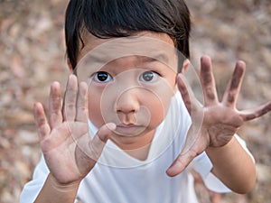 Asian cute little child boy showing dirty black hands while playing outdoor.