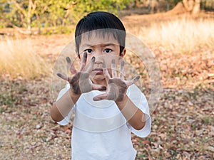 Asian cute little child boy showing dirty black hands while playing outdoor. Happy kid enjoy in relaxing day