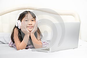 Asian Cute little girl wear headphones to learn online using a laptop in the bedroom