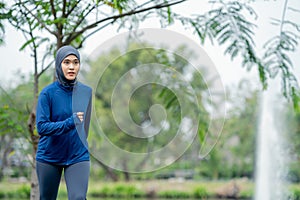 Asian cute muslim woman wearing sportswear and a blue hijab Exercising and running outdoors at the park in the morning.