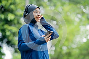 Asian cute muslim woman wearing sportswear and a blue hijab Working out and wearing earphones listening to music