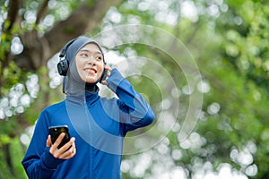 Asian cute muslim woman wearing sportswear and a blue hijab Working out and wearing earphones listening to music