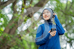 Asian cute muslim woman wearing sportswear and a blue hijab Working out and wearing earphones listening to music