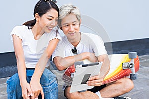 Asian cute woman sitting on skateboards, handsome man sitting on street around skateboard way, smile, and they are happy using