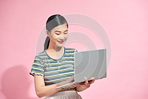 Asian cute young woman smiling standing using laptop computer on hand looking to computer isolated