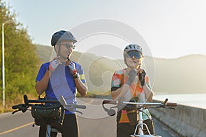 Asian cyclist couple dons helmets and chin straps as they prepare for their bike ride around a beautiful morning lake