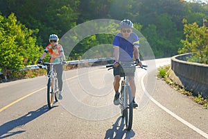 Asian cyclist couple riding together for exercise around the lake in the morning with beautiful mountain view in the background