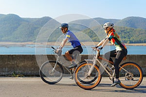 Asian cyclist couple riding together for exercise around the lake in the morning with beautiful mountain view in the background