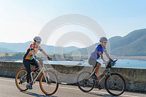 Asian cyclist couple riding together for exercise around the lake in the morning with beautiful mountain view in the background