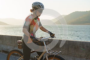 Asian cyclist woman prepares for exercise bike around the lake in the clear morning
