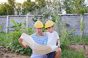 Asian Dad and son wearing yellow construction helmet standing in front of construction site