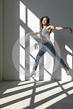 Asian dancer girl makes an acrobatic jump illuminated by the sun that enters through the window in an empty building.