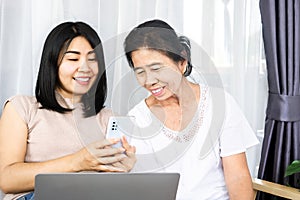 Asian daughter with old mother using mobile phone and laptop sharing technology together