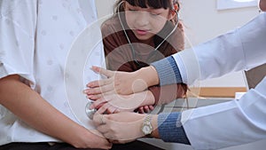 Asian daughter using stethoscope listening baby heartbeat with mother while doctor by side at hospital.