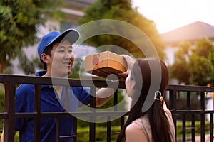 Asian delivery man in blue shirt sending parcel box to home while young woman receiving a package in front of custoomer