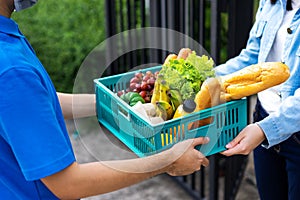 Asian delivery man blue uniform wearing medical face mask making grocery service giving fresh food to customer receiving front hou