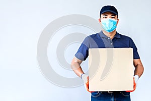 Asian delivery man employee in blue cap blank t-shirt uniform face mask gloves hold empty cardboard box isolated on white