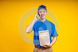 Asian delivery man holding parcel box over yellow isolate background