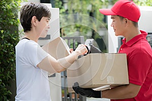 Asian delivery man in red uniform delivering parcel box to woman recipient at home with recipient sign to receive the package on s