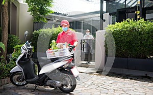 Asian delivery man wearing face mask and gloves in red uniform delivering  groceries box of food, fruit, vegetable and drink to re