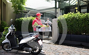 Asian delivery man wearing face mask and gloves in red uniform delivering  groceries box of food, fruit, vegetable and drink to re