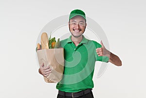 Asian delivery man wearing in green uniform holding fresh food paper bag groceries and thumbs up isolated over white background.