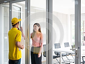 Asian delivery man who wear yellow uniform with cap hold confidential document in craft paper and knock the window for send