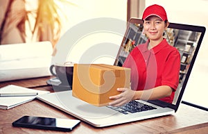 Asian delivery woman in red shirt with blur warehouse background, holding goods order in package parcel out from laptop computer.