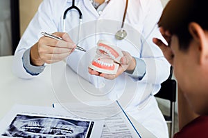 Asian dentist holding pen pointing to the dentures and is describing the problem of teeth.