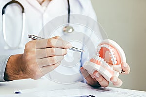 Asian dentist holding pen pointing to the dentures and is describing the problem of teeth