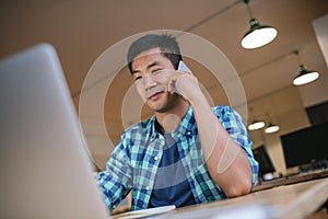 Asian designer using a laptop and talking on his cellphone