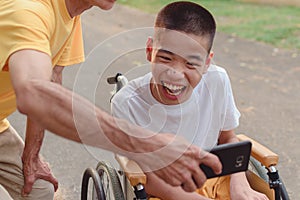 Asian Disabled child and adult on wheelchair in city park,They have fun with selfie by smart phone