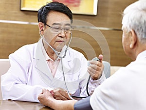 Asian doctor checking blood pressure of a senior patient