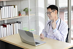 Asian doctor examining hold a hand near his neck, finger pressures for showing patient through online video chat with computer in