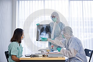 Asian doctor in personal protective equipment or ppe explain the x-ray film of covid-19 or coronavirus infection to patient