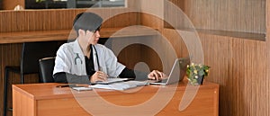 An Asian doctor sits at his desk works on laptop computer