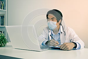 Asian Doctor and Stethoscope Wear Face Mask Write Experimental Results Report and Using Laptop Computer in Vintage Tone