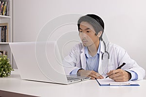 Asian Doctor and Stethoscope Write Experimental Results Report and Using Laptop Computer