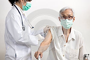 Asian doctor with syringe doing injection of vaccine,nurse vaccinating elderly in the hospital,vaccination to old senior at risk photo