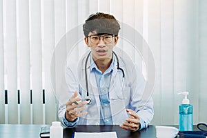 Asian doctor wearing glasses and white uniforms with a stethoscope provides online counseling to patients during the virus