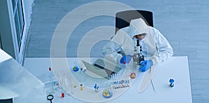 Asian doctor wearing protective white jumpsuit and face mask with glasses testing sample with microscope in clinical