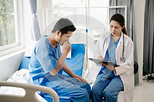 Asian doctor in white suit take notes while discussing and Asian elderly, man patient who lying on bed with receiving saline