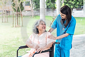 Asian doctor woman looking and taking care elderly woman patient with paralysis, is sitting on a wheelchai