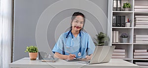 Asian doctor young beautiful woman smiling using working with a laptop computer and her writing something on paperwork