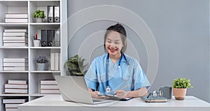 Asian doctor young beautiful woman smiling using working with a laptop computer and her writing something on paperwork